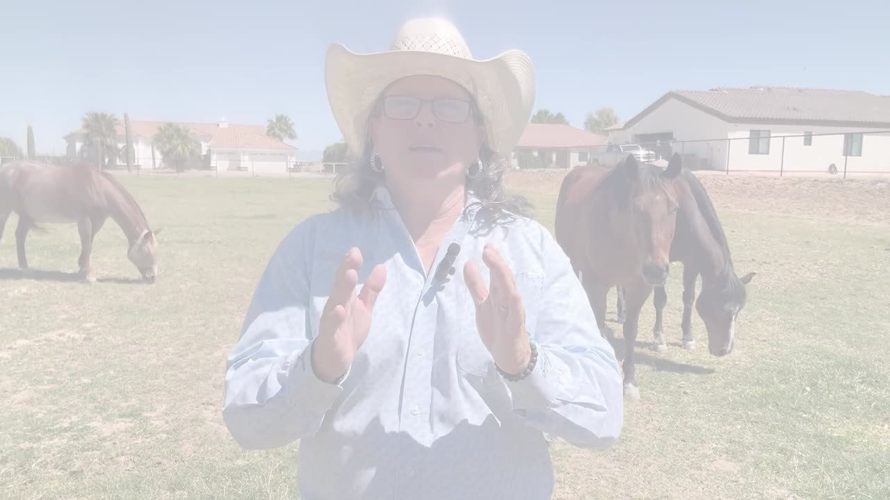 Kim Williamson in a white cowboy hat with horses behind her